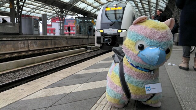 A giant alpaca horse in front of a class 462 / Siemens Desiro HC entering a station.