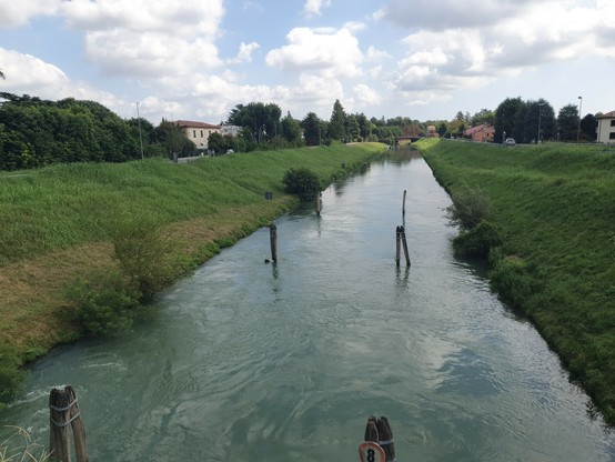 Ein Kanal mit Deichen an beiden seiten. Im Kanal stehen vier Pfosten.